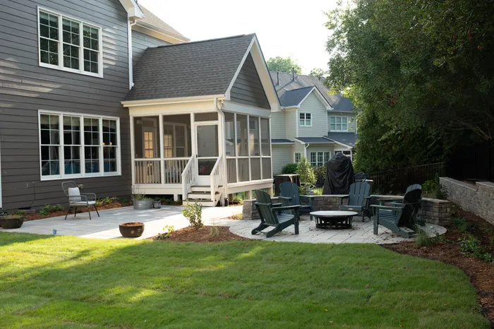 Paver patio with a stone fire pit seating area beside a screened porch in an Apex backyard