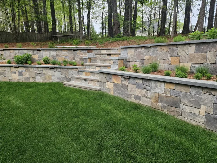 Tiered natural stone retaining walls with built-in steps in a wooded backyard